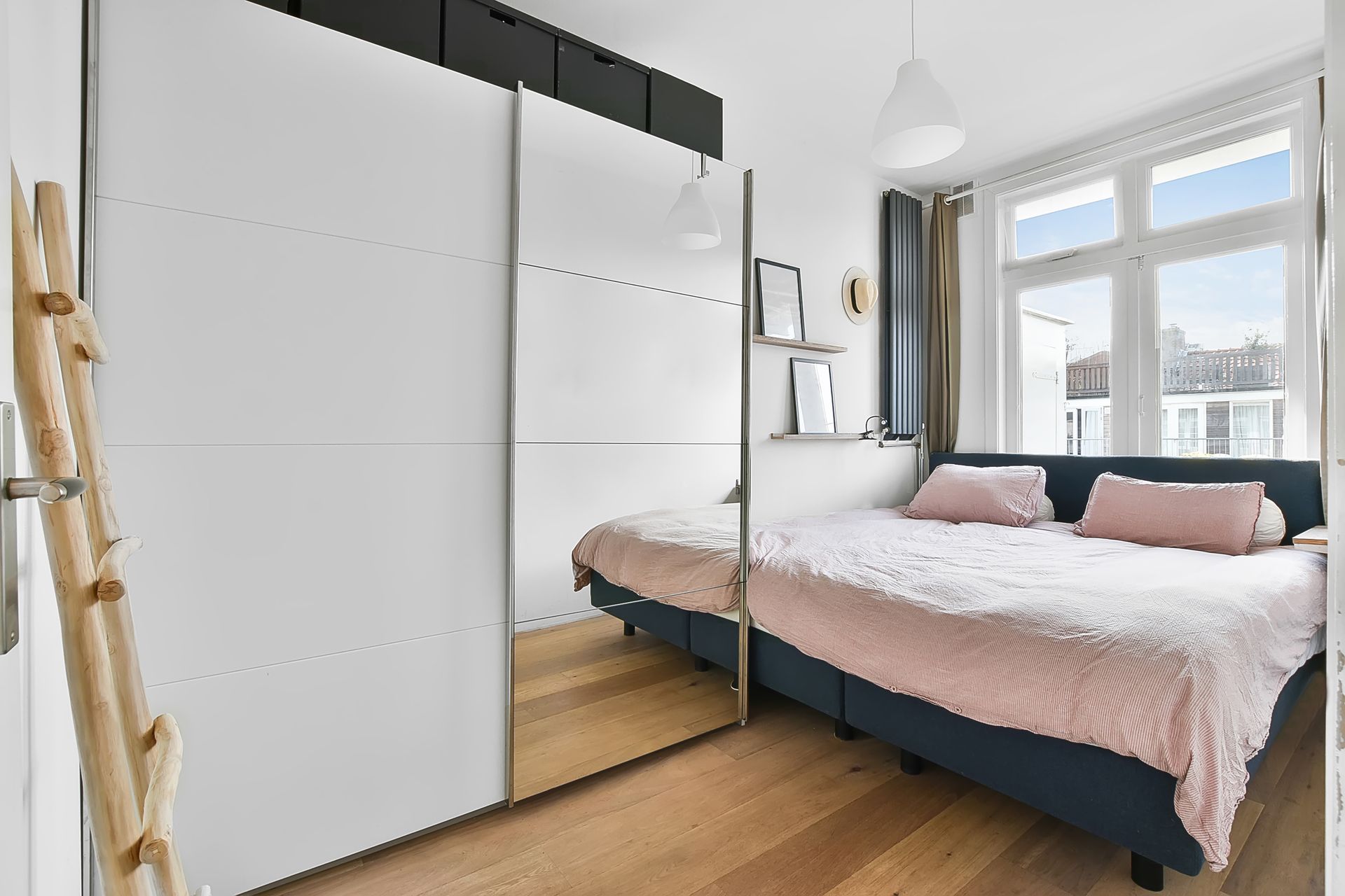 Bedroom with mirrored closet, bed, window, and wood floor.