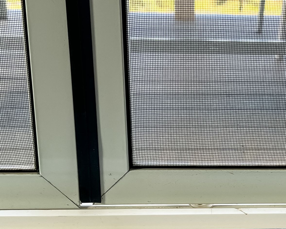 Close-up of a white window frame with a black screen and thin vertical black strip.