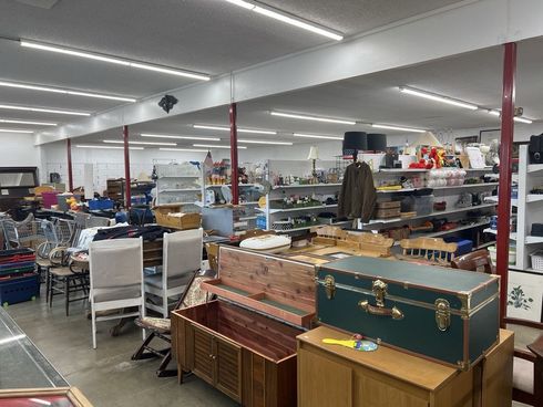 Interior of a cluttered thrift store, filled with furniture, shelves, and various items.