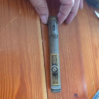 Person holding a worn, vintage spirit level with a brass top and label on wooden surface.