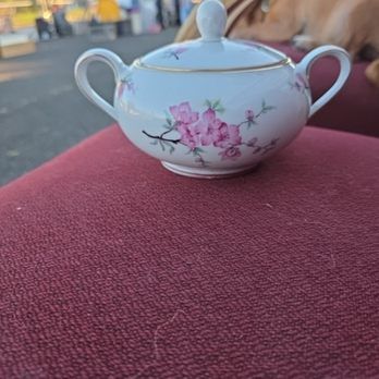 A floral-decorated sugar bowl with lid sits on a red fabric surface.