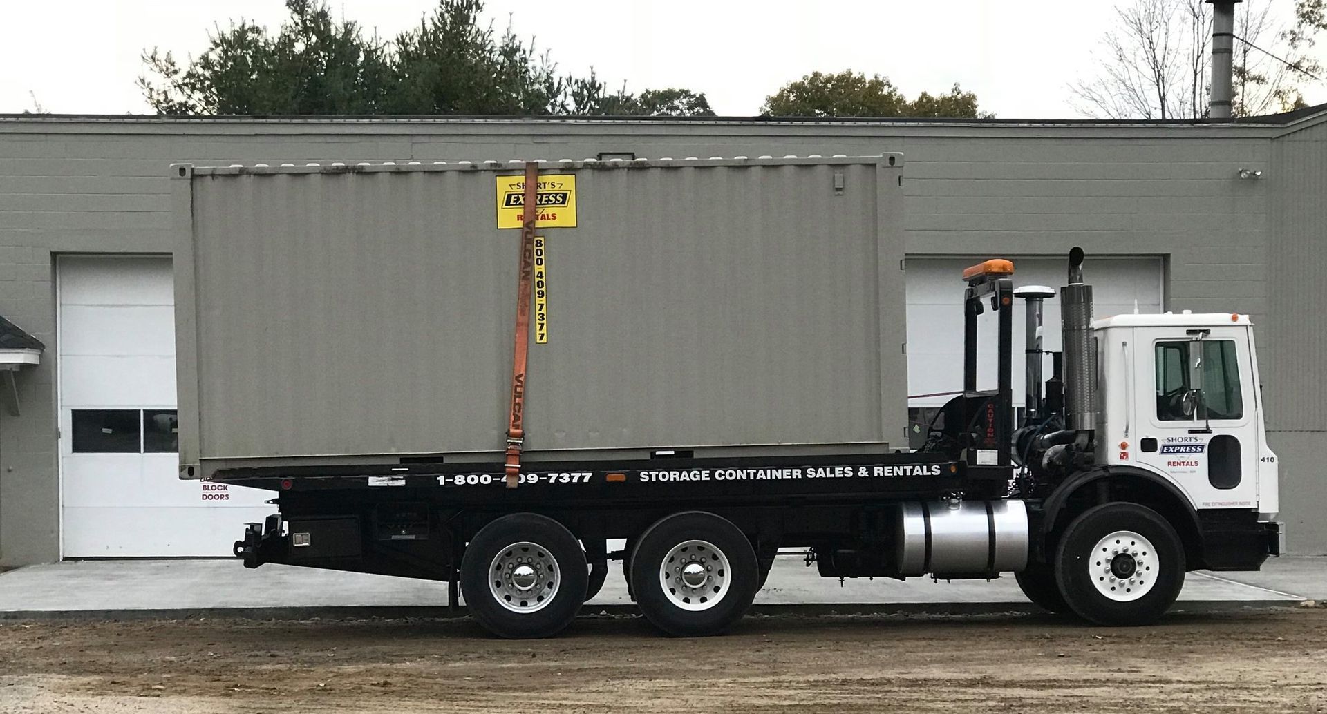 A truck with a container on the back is parked in front of a garage.