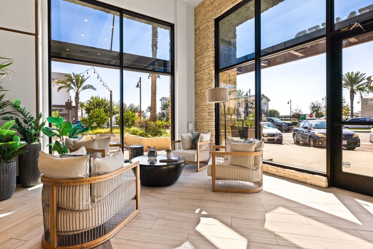 Bright community lounge with floor-to-ceiling windows, beige seating, and potted plants.
