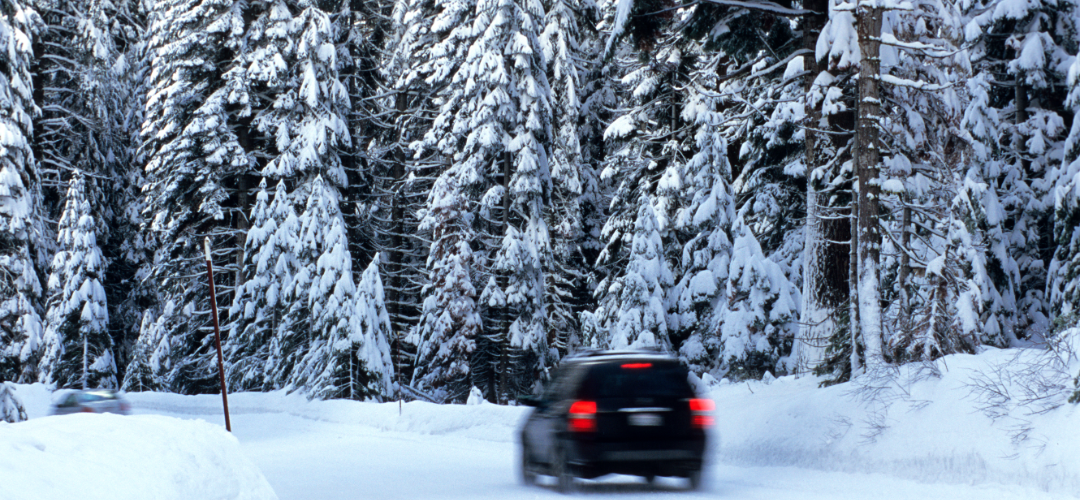A car is driving down a snowy road in the woods
