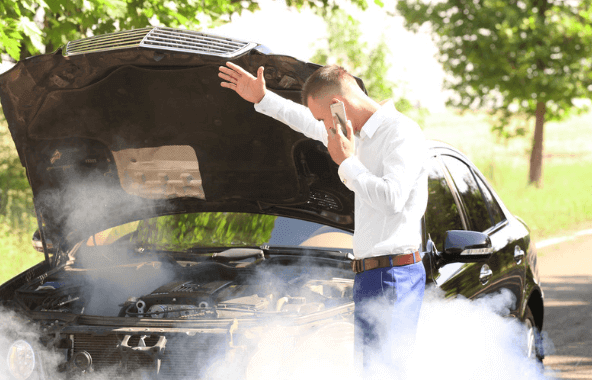 A man is talking on a cell phone in front of a broken down car.
