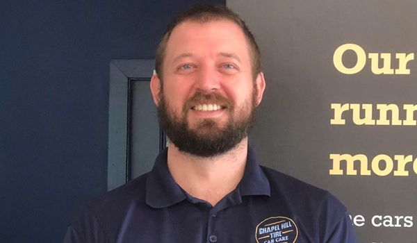 A man with a beard is smiling in front of a sign that says our run more cars
