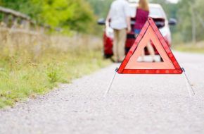 A red triangle is sitting on the side of the road next to a broken down car.