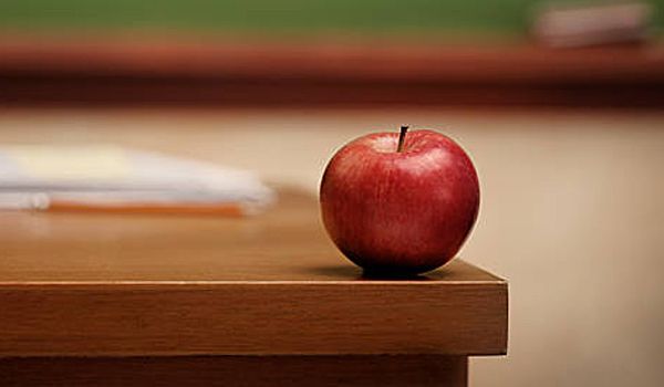 A red apple is sitting on top of a wooden desk.