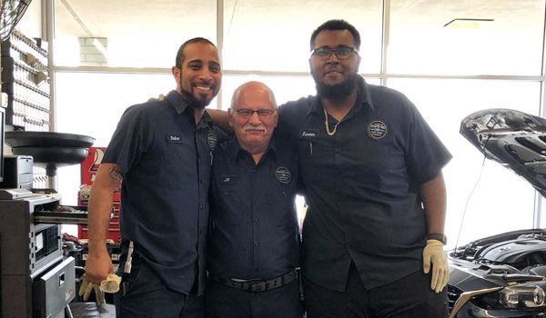 Three men are posing for a picture in front of a car.