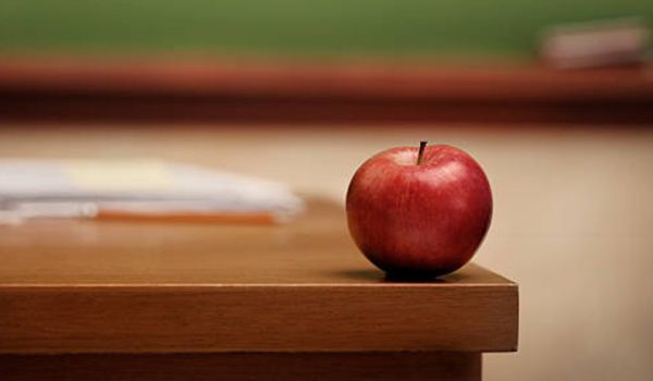 A red apple is sitting on top of a wooden desk.