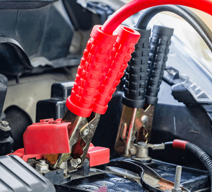 A close up of a car battery with red jumper cables attached to it