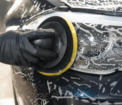 A person is polishing the headlight of a car