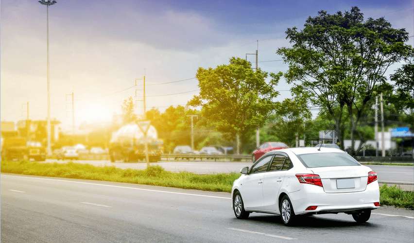 A white car is driving down a road with trees in the background
