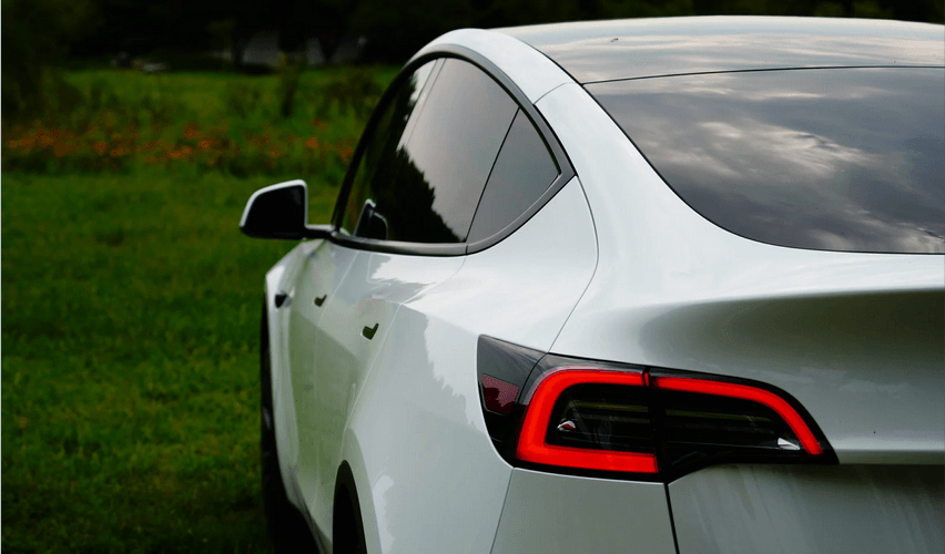 A white tesla model 3 is parked in a grassy field