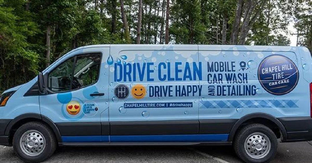 A blue van is parked in a parking lot with trees in the background.