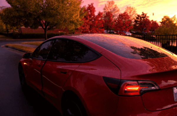 A red tesla model 3 is parked in front of a sunset