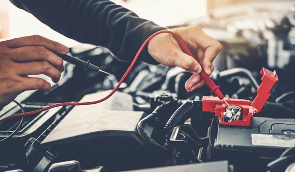 A person is working on a car battery with a multimeter.
