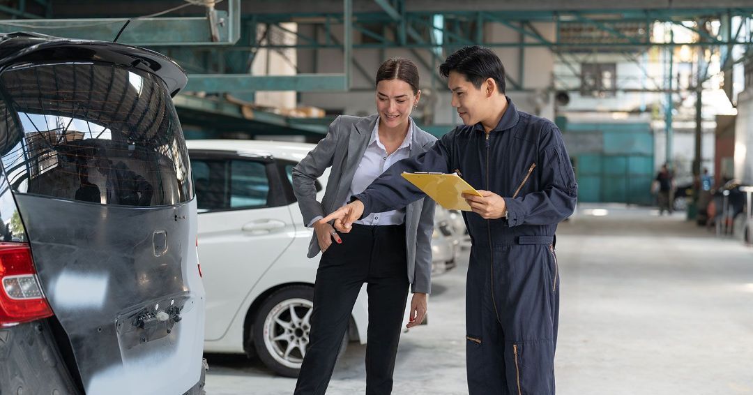 A man and a woman are looking at a car in a garage.