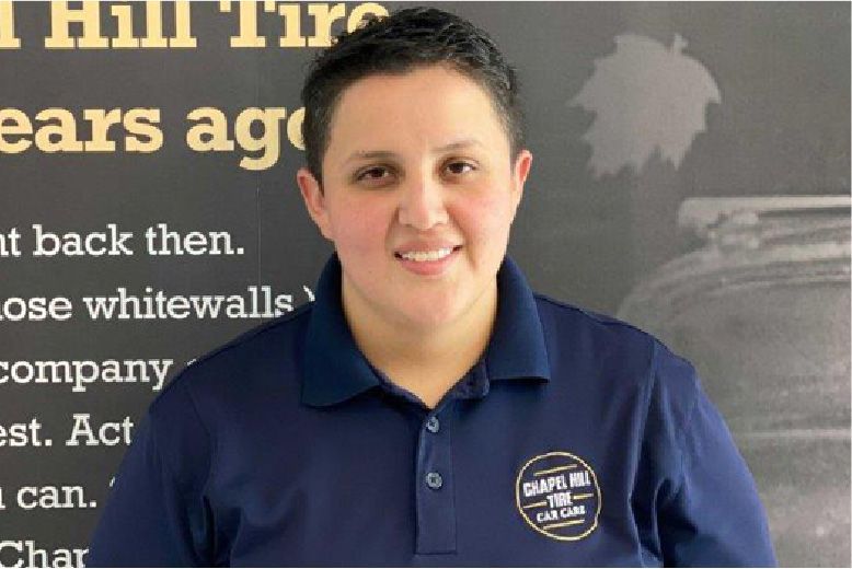 Woman in blue shirt with logo in front of a black sign about Hill Tire.