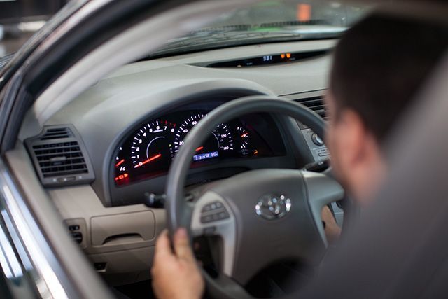A man is driving a toyota car and looking at the dashboard