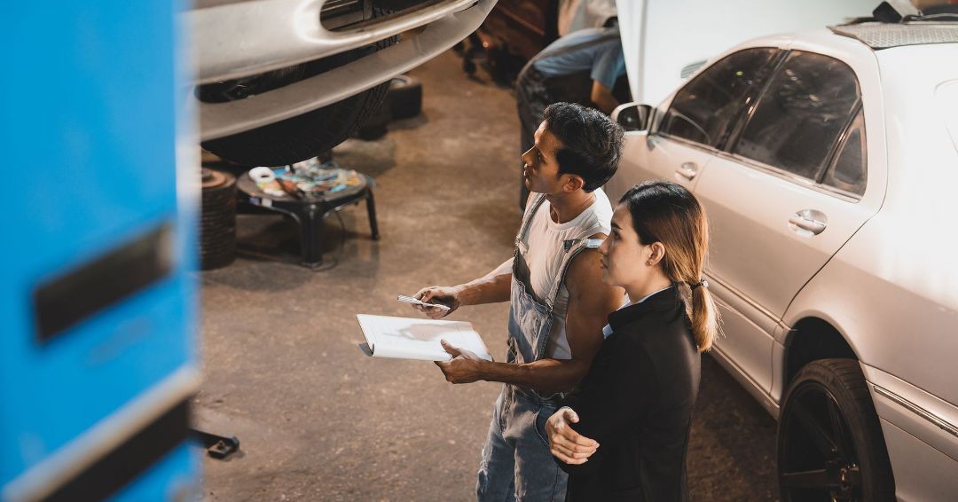 A man and a woman are looking at a car in a garage.
