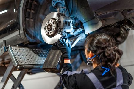 Mechanic working on car brakes; holding light, in a garage.