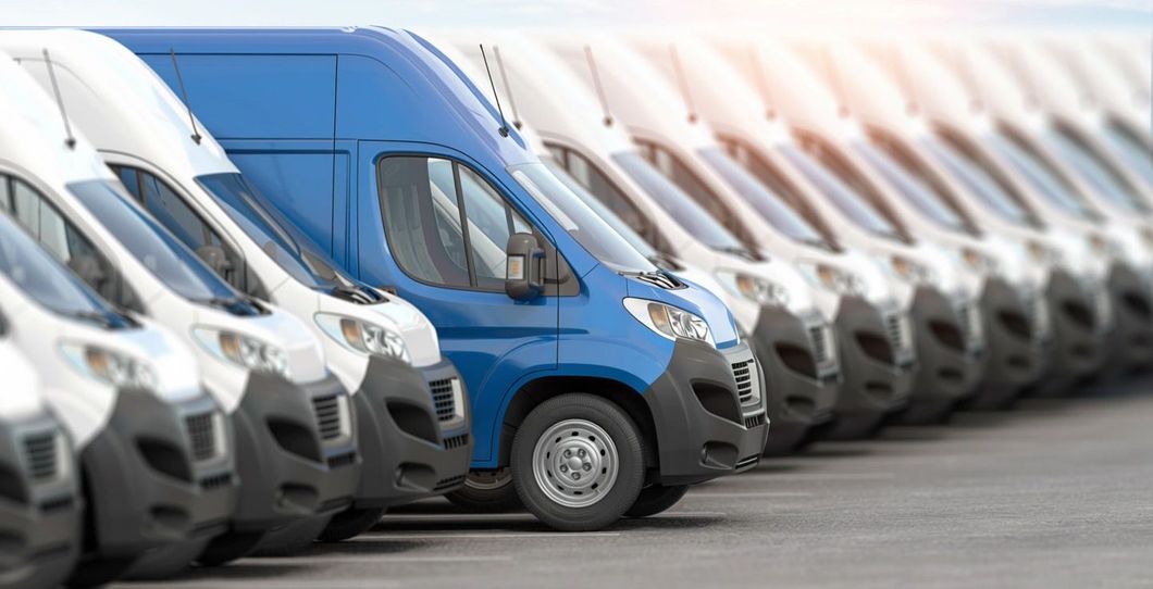 Row of white vans with one blue van, parked outside.