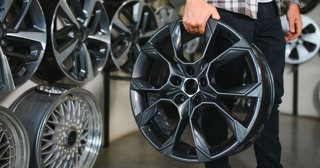 A man is holding a car wheel in his hand in a store.