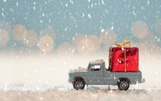 A toy truck is carrying a red gift box in the snow.