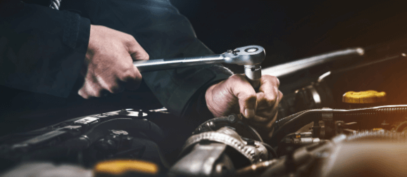 A man is working on a car engine with a wrench.