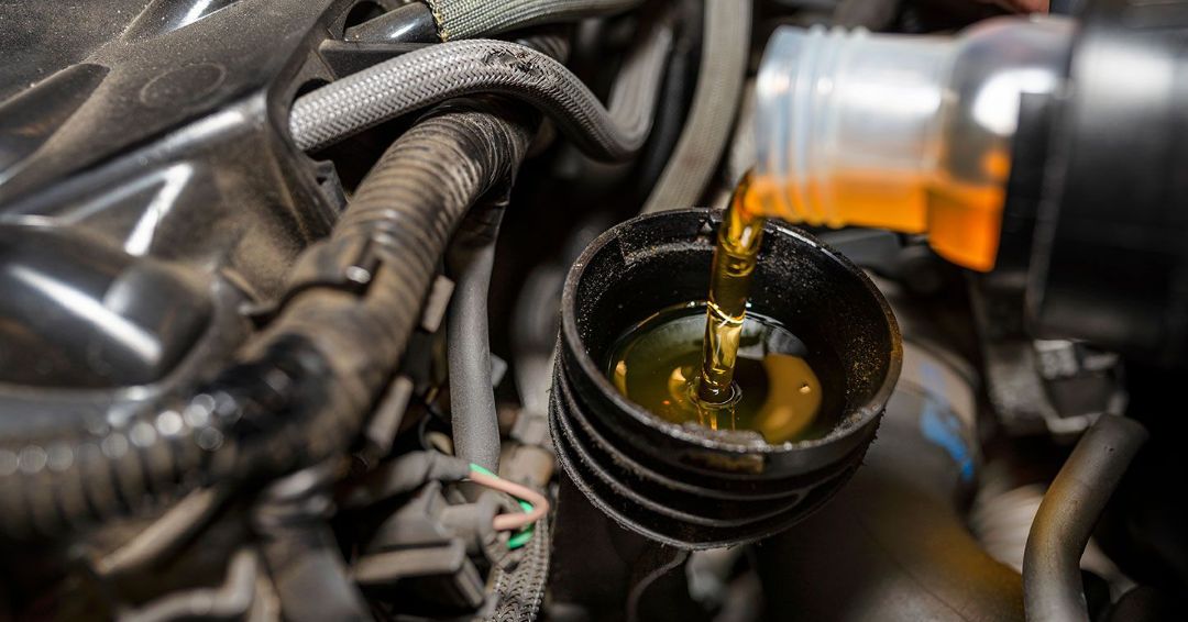 A close up of a car engine with oil being poured into a bucket.