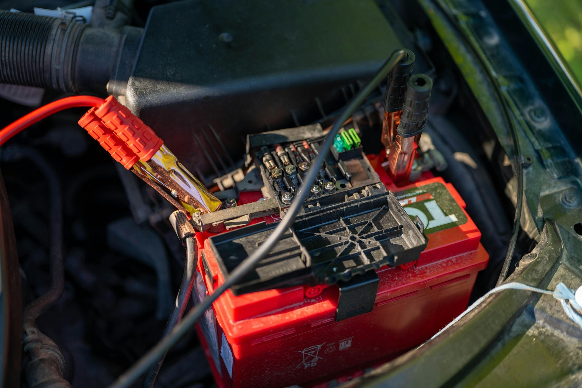 Car battery being jumped with red and black jumper cables.