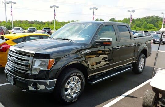 Black Ford F-150 pickup truck parked in a lot on a sunny day. Chrome accents, side steps, and wheels.