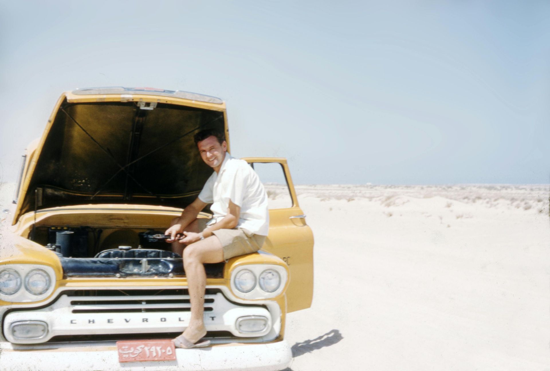 A man is sitting on the hood of a yellow chevrolet truck