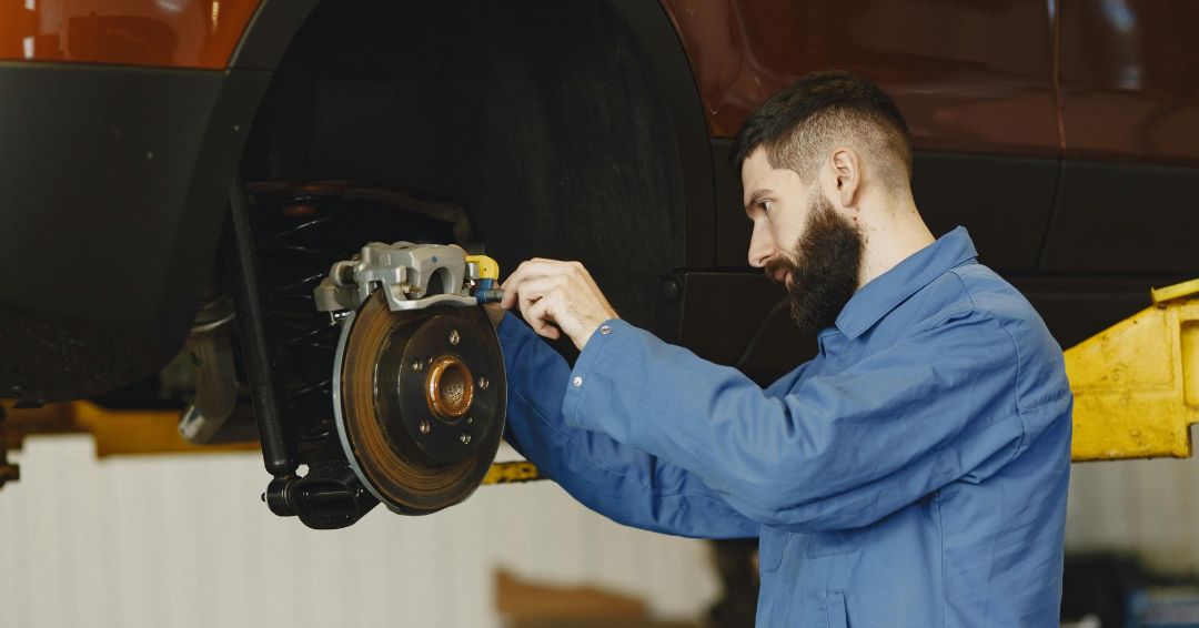 A man is working on a car on a lift in a garage.