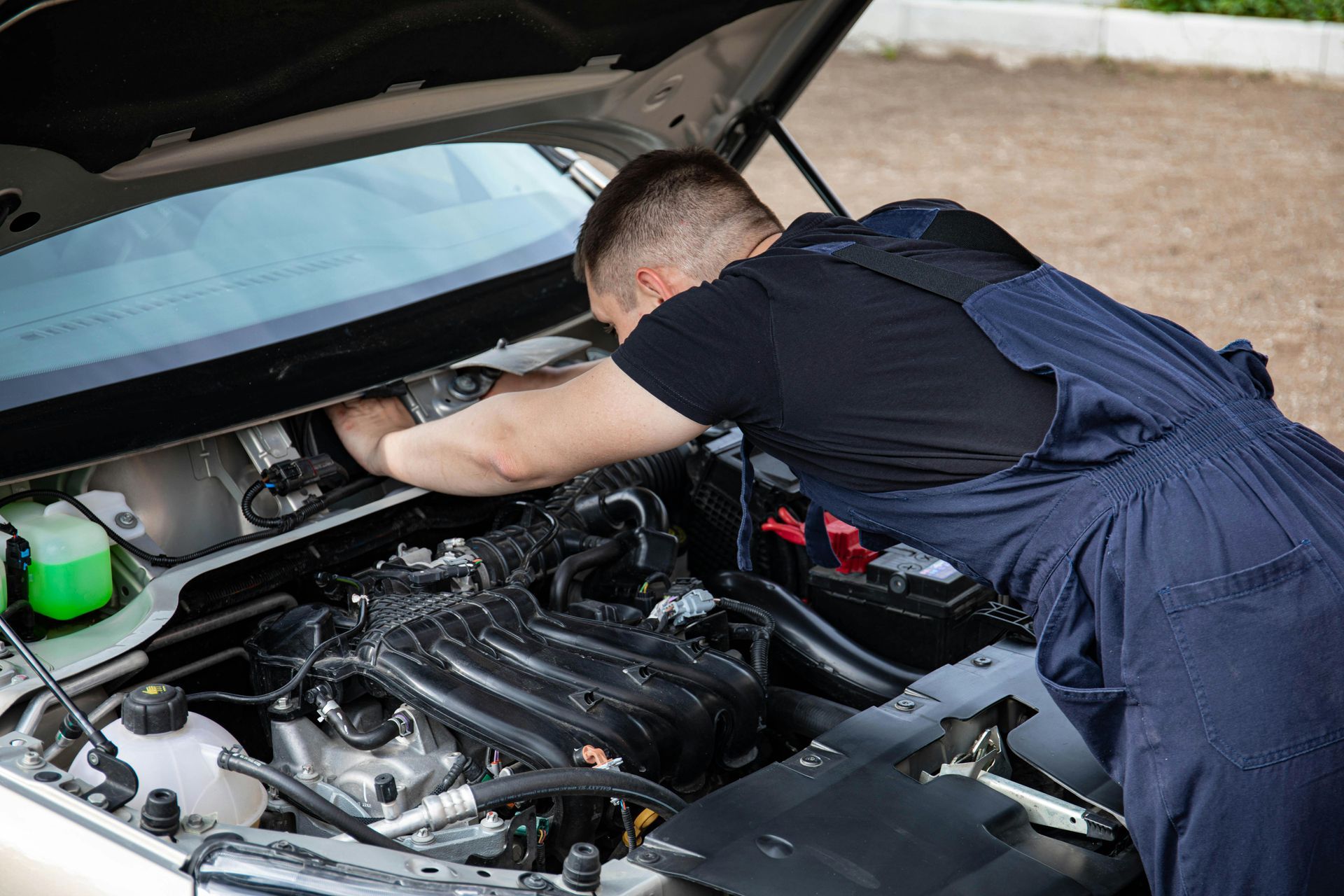 Mechanic leaning into a car’s open hood, inspecting the engine bay.