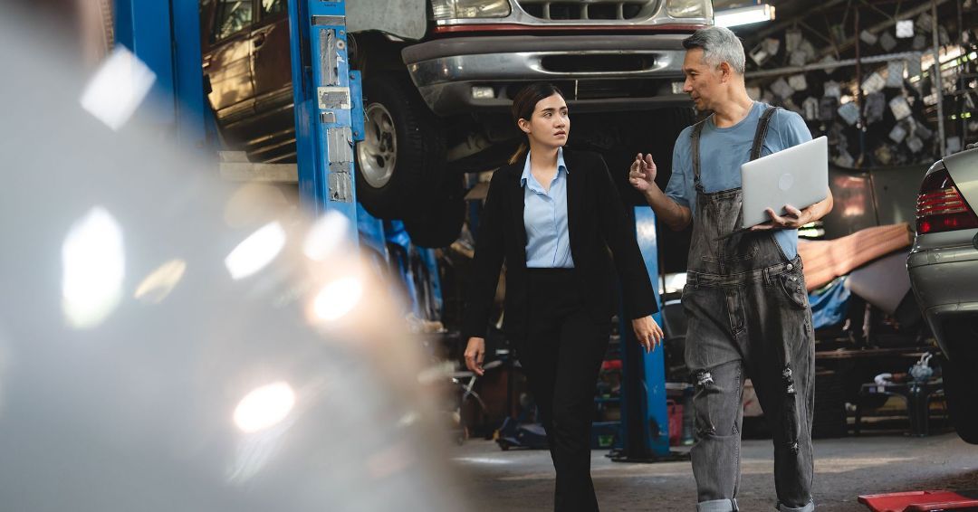 A man and a woman are standing in a garage talking to each other.