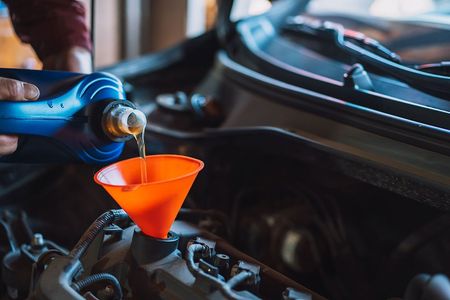 Pouring motor oil into a car engine with an orange funnel in an automotive shop.