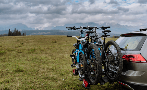 A car with three bikes attached to it is parked in a grassy field.