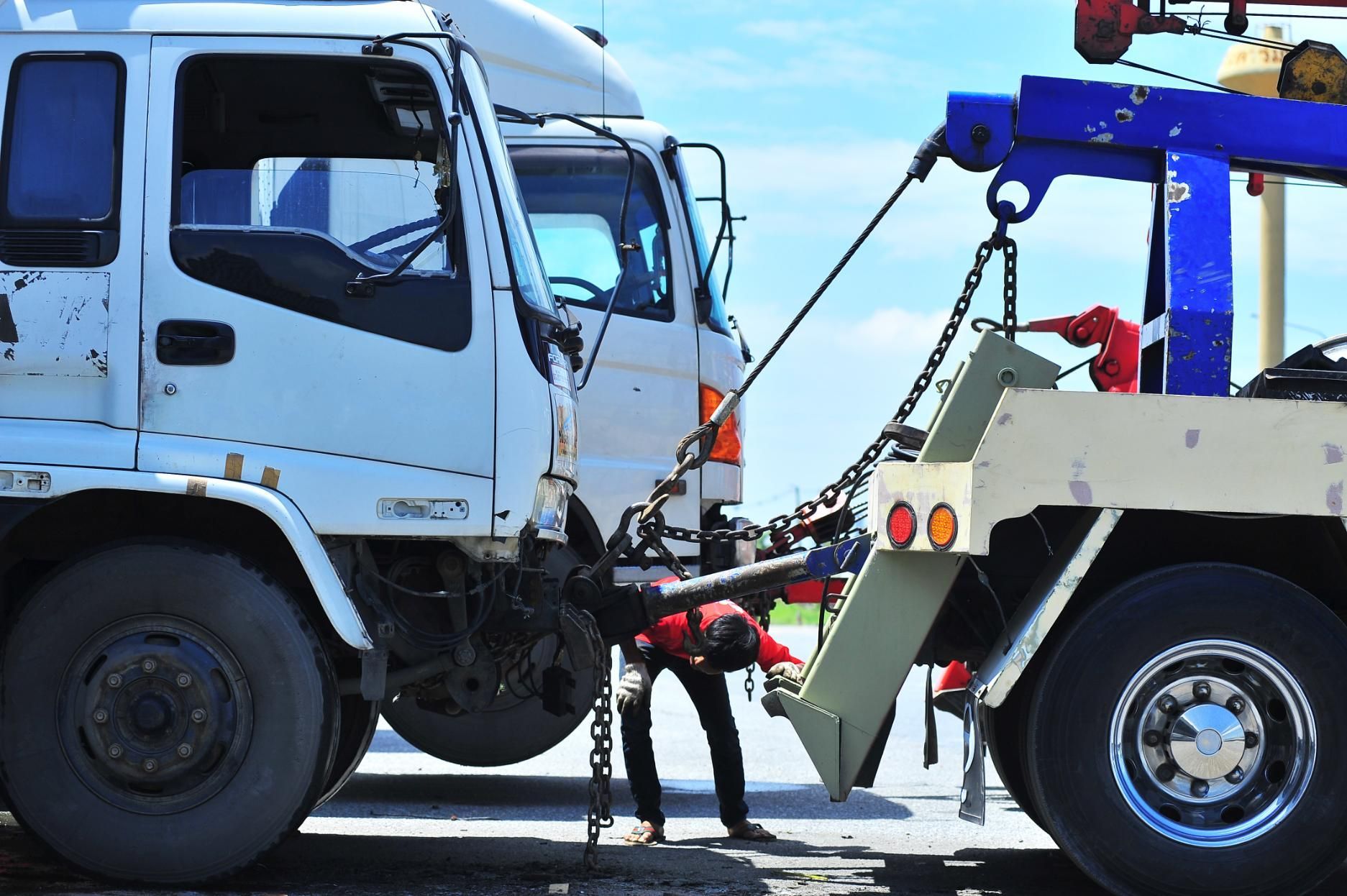 A man is working on a tow truck that is being towed by another truck.