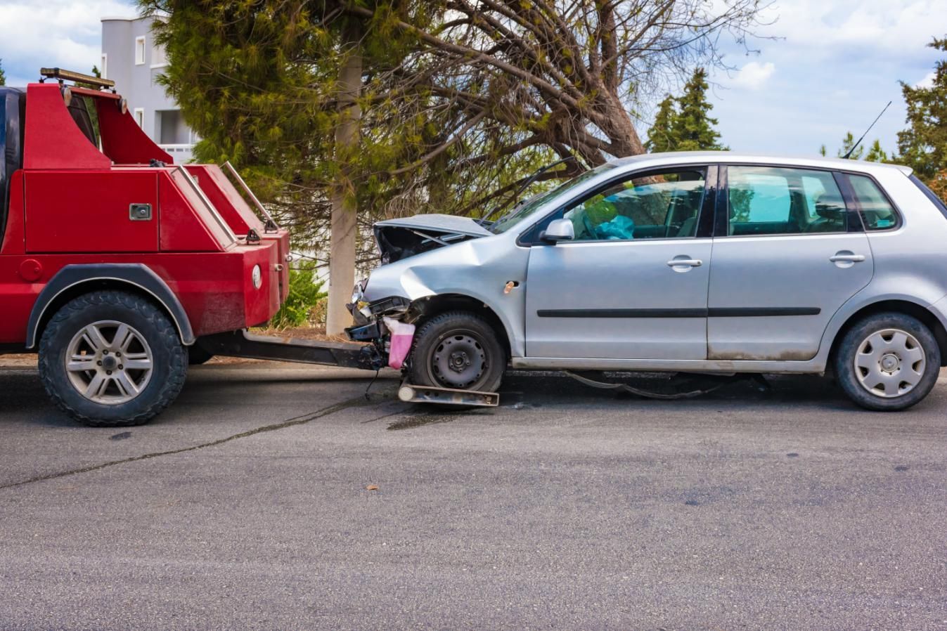 A tow truck is towing a damaged car on the street.