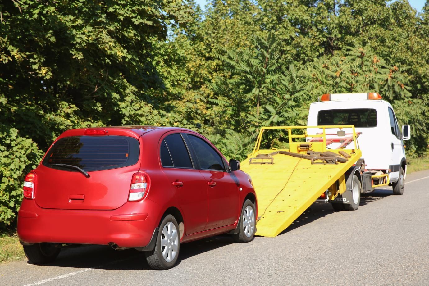 A red car is being towed by a tow truck.