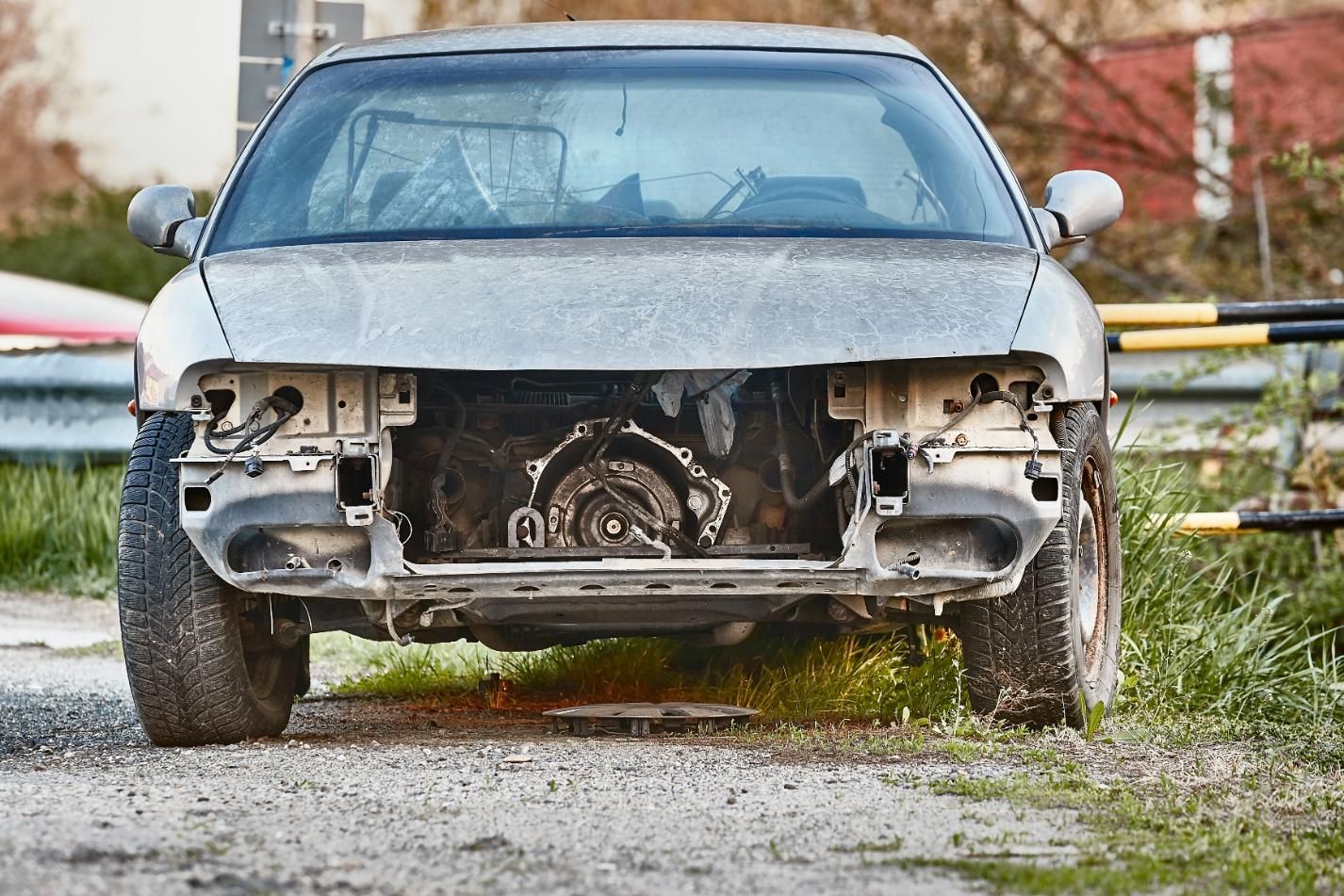 A gray car with the hood removed is parked on the side of the road.