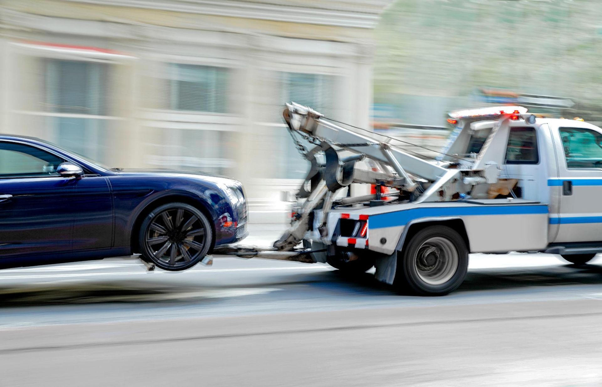 A blue car is being towed by a tow truck.