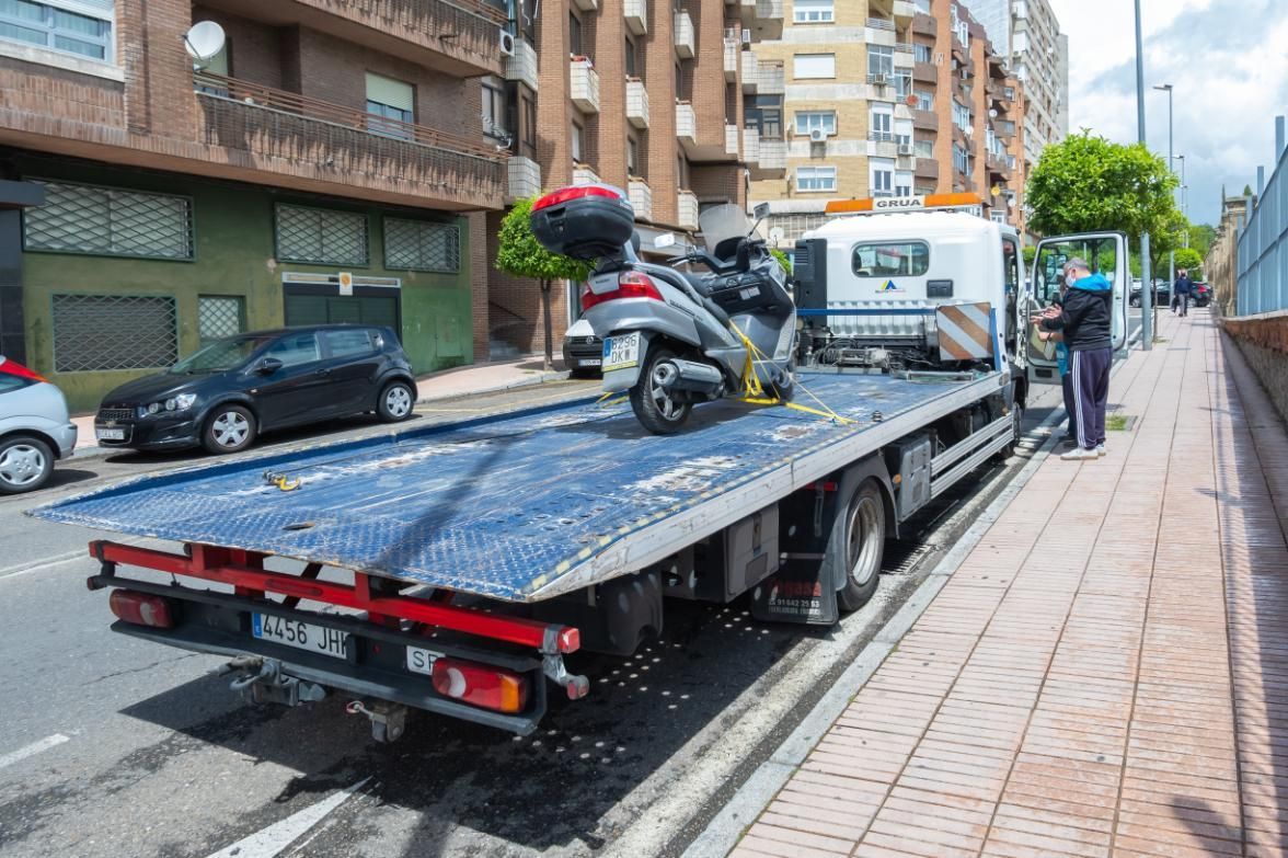 A tow truck with a motorcycle on the back is parked on the side of the road.