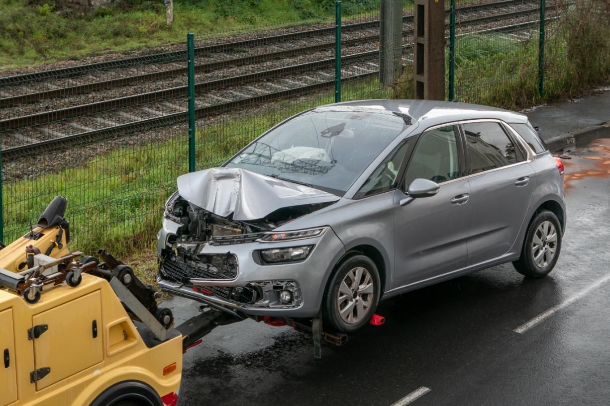 A tow truck is towing a damaged car on the side of the road.
