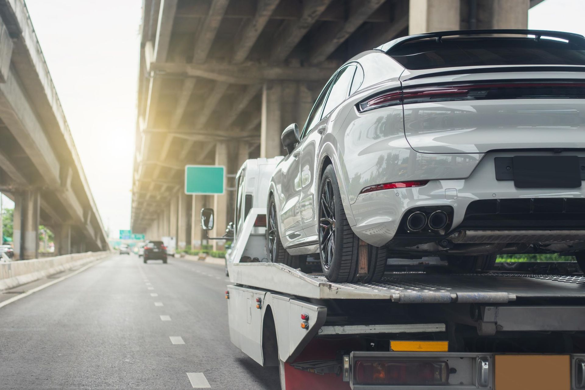 A white car is being towed down a highway by a tow truck.