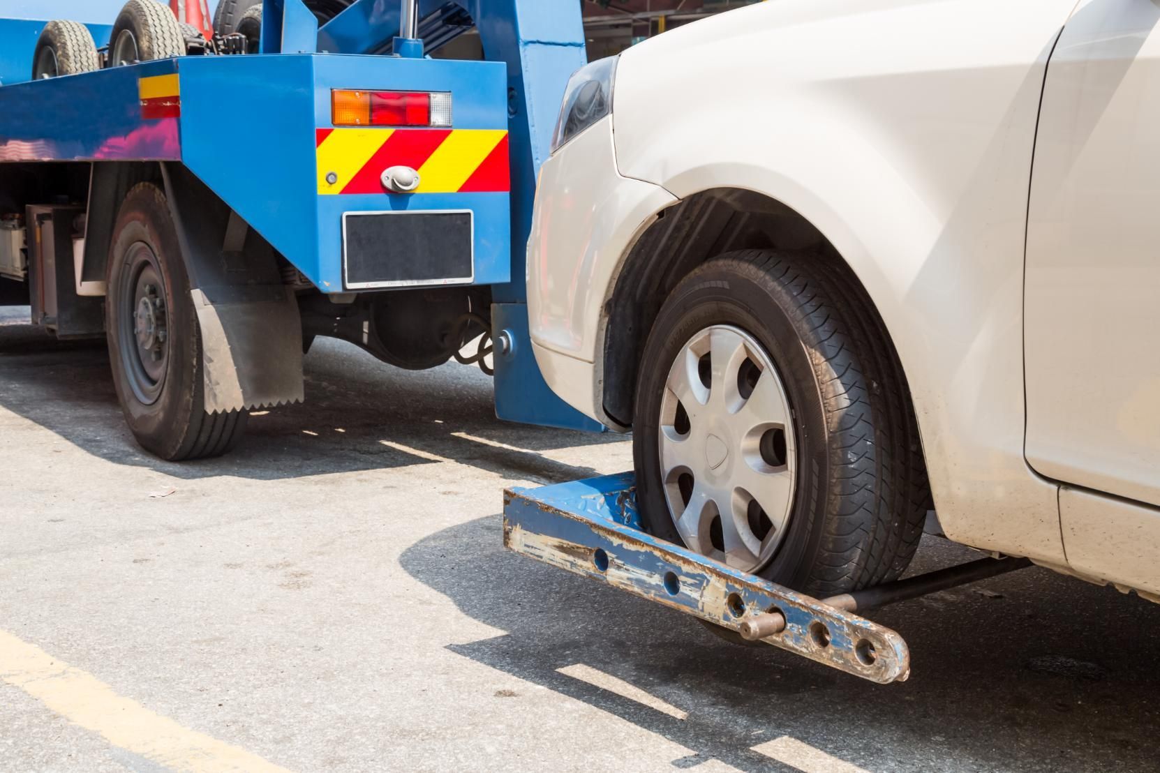 A white car is being towed by a blue tow truck.