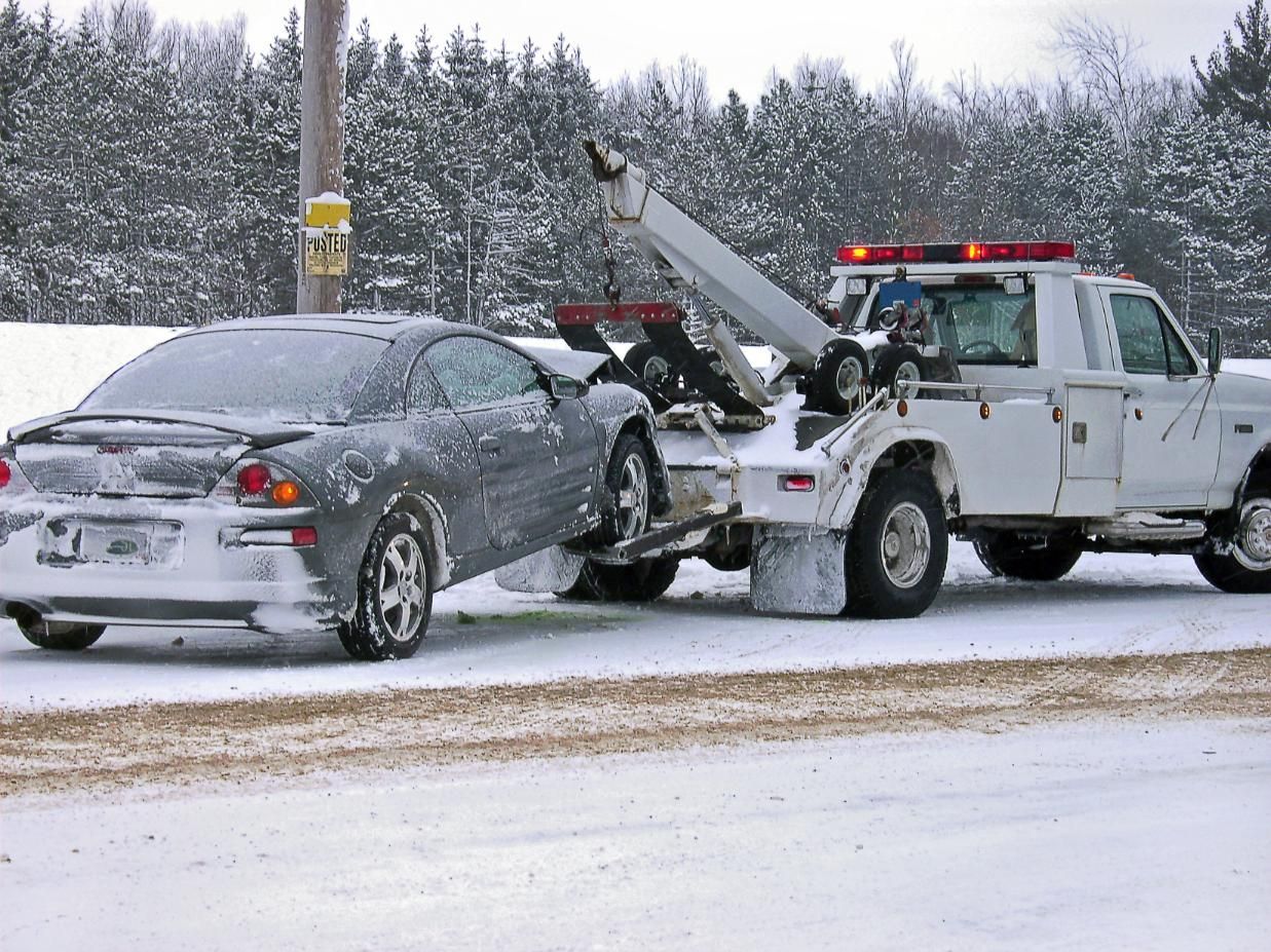 A car is being towed by a tow truck in the snow.