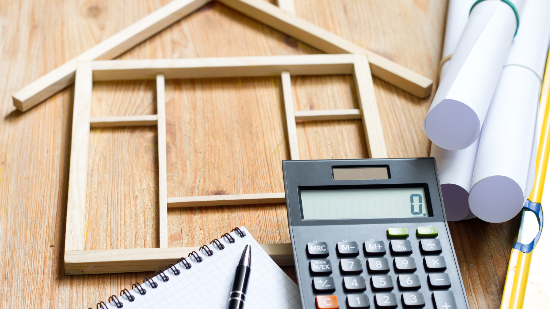 A calculator is sitting on a wooden table next to a model of a house.